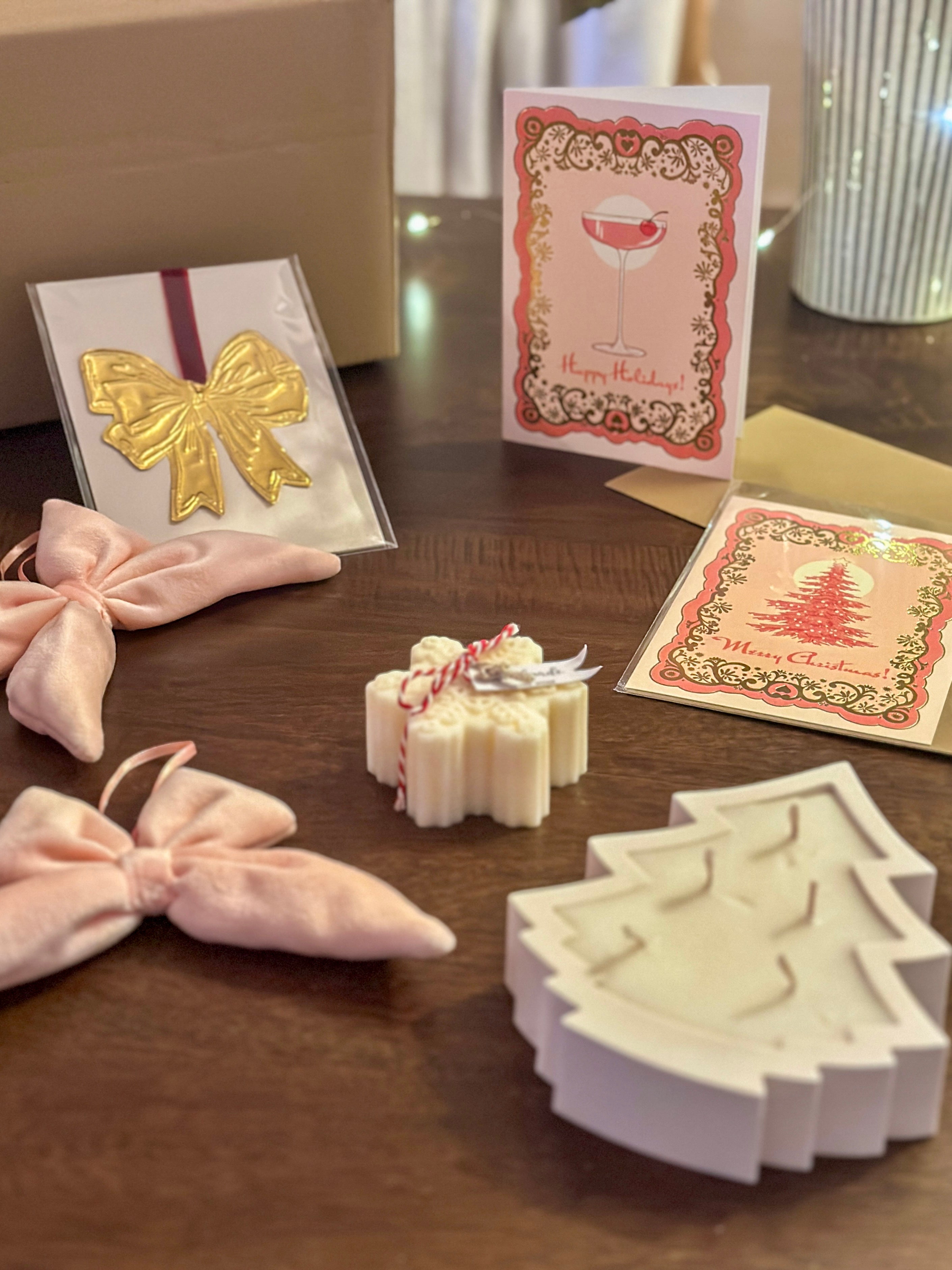 Feminine-themed Christmas box with pink velvet bows, tin ornaments, scented candles, and luxe gold foil-stamped Christmas cards. Perfect for holiday gifting.