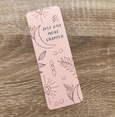 Boho-themed waterproof bookmark with "Just One More Chapter" text, featuring illustrations of moons, leaves, and abstract shapes in pink and brown tones. Made from recycled card with a velvet lamination.