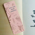 Boho-themed waterproof bookmark with "Just One More Chapter" text, featuring illustrations of moons, leaves, and abstract shapes in pink and brown tones. Made from recycled card with a velvet lamination.