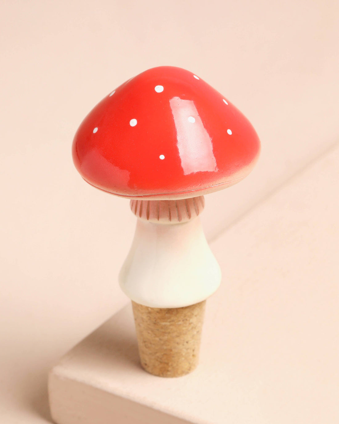 Mushroom-shaped bottle stopper with red cap and white body on a beige background