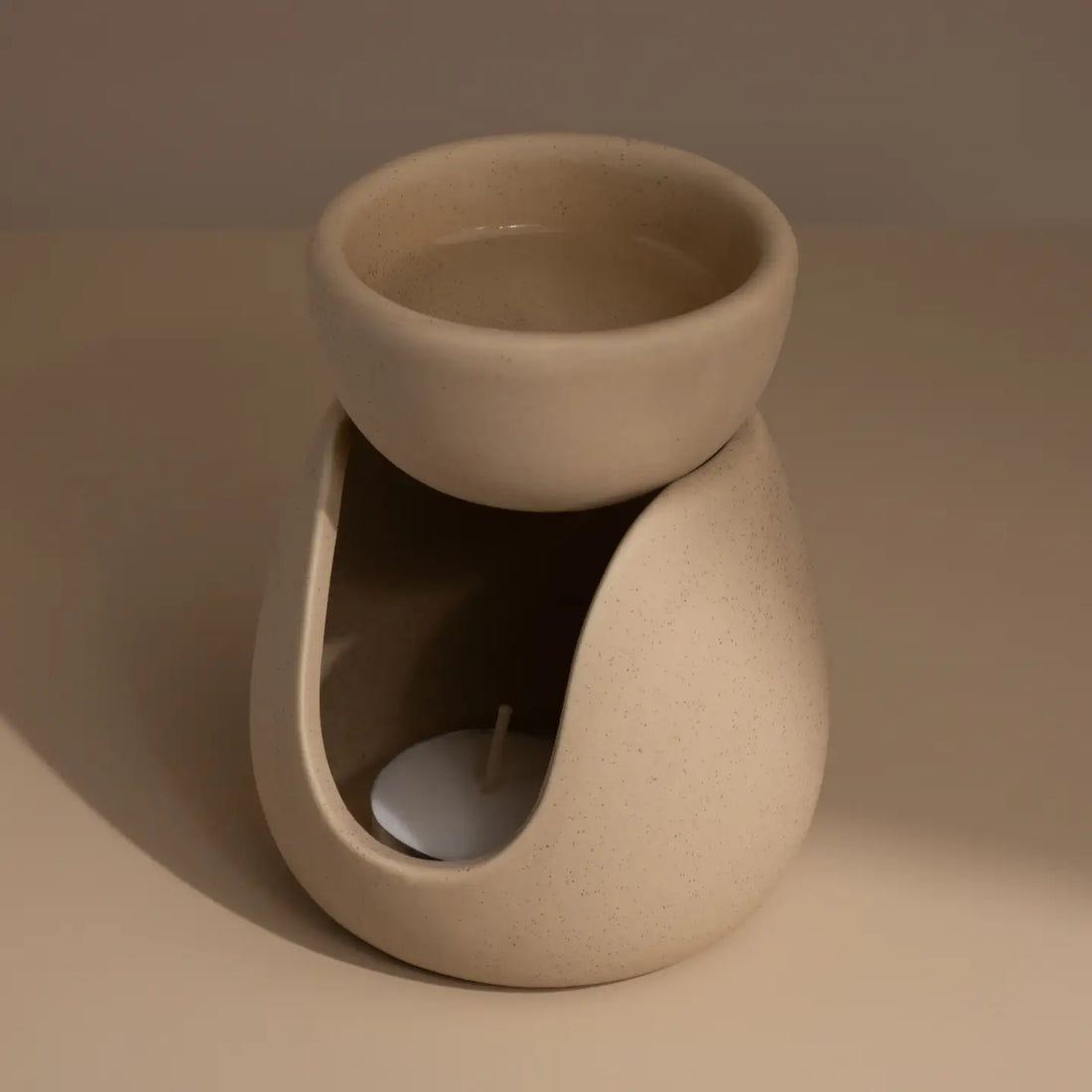 Beige ceramic wax melt burner with tea light on a neutral table and background