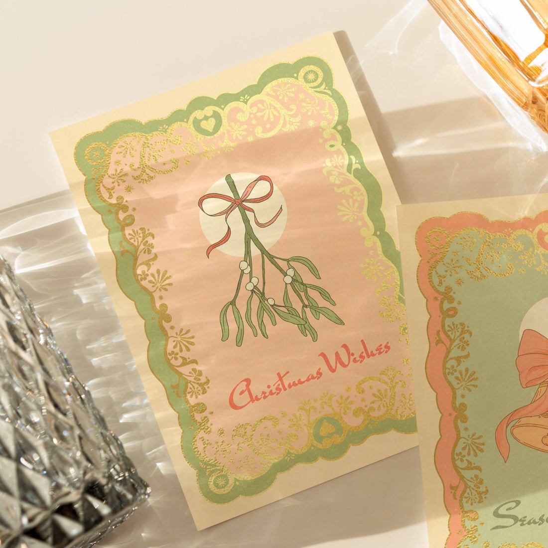 A6 handmade eco-conscious card with a soft pink background, green mistletoe accents, and luxe gold foil. Includes a Kraft envelope and biodegradable cello wrap.