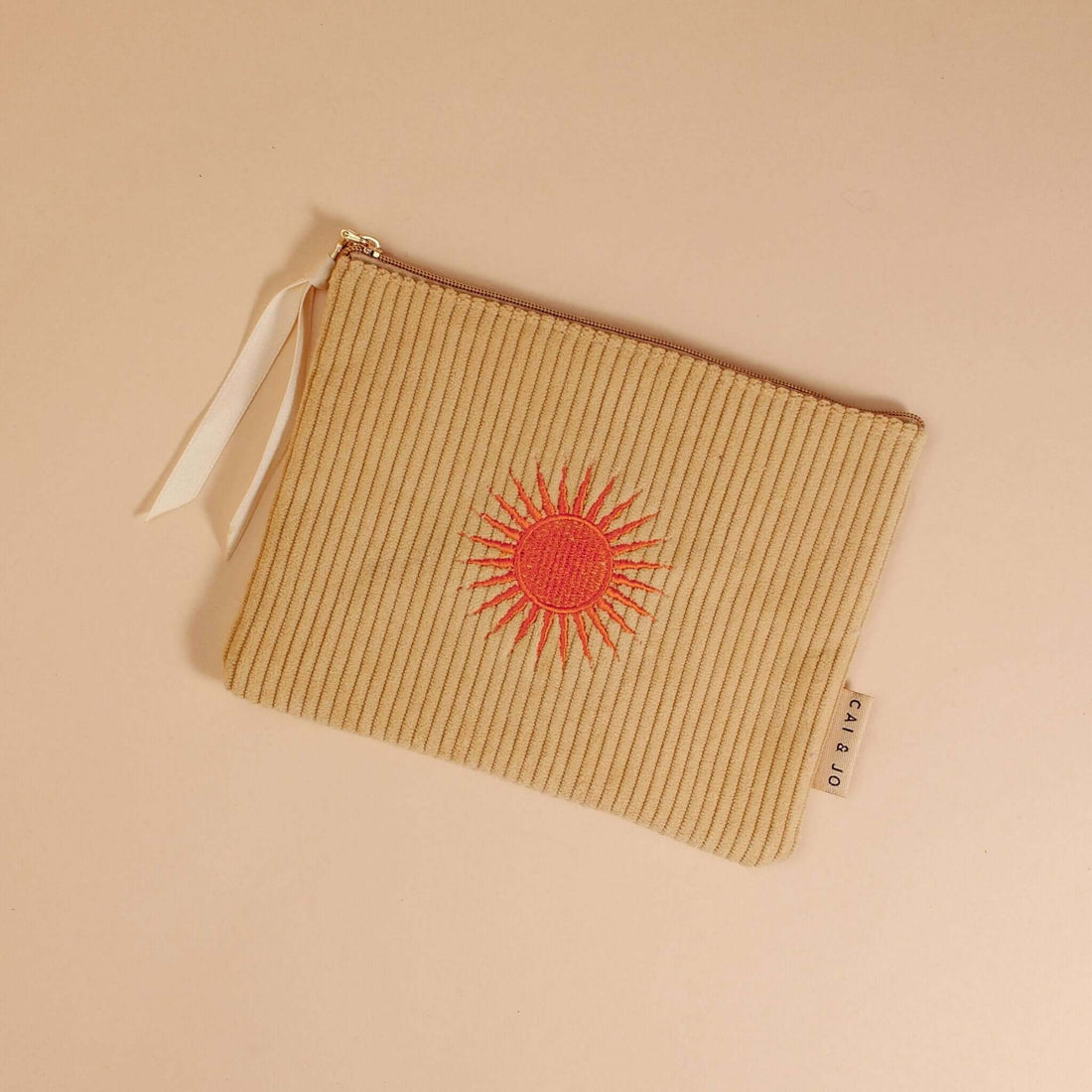 Pale ochre corduroy pouch with a zip closure, fully lined, and an orange sun design. Perfect for storing makeup, toiletries, or travel essentials.