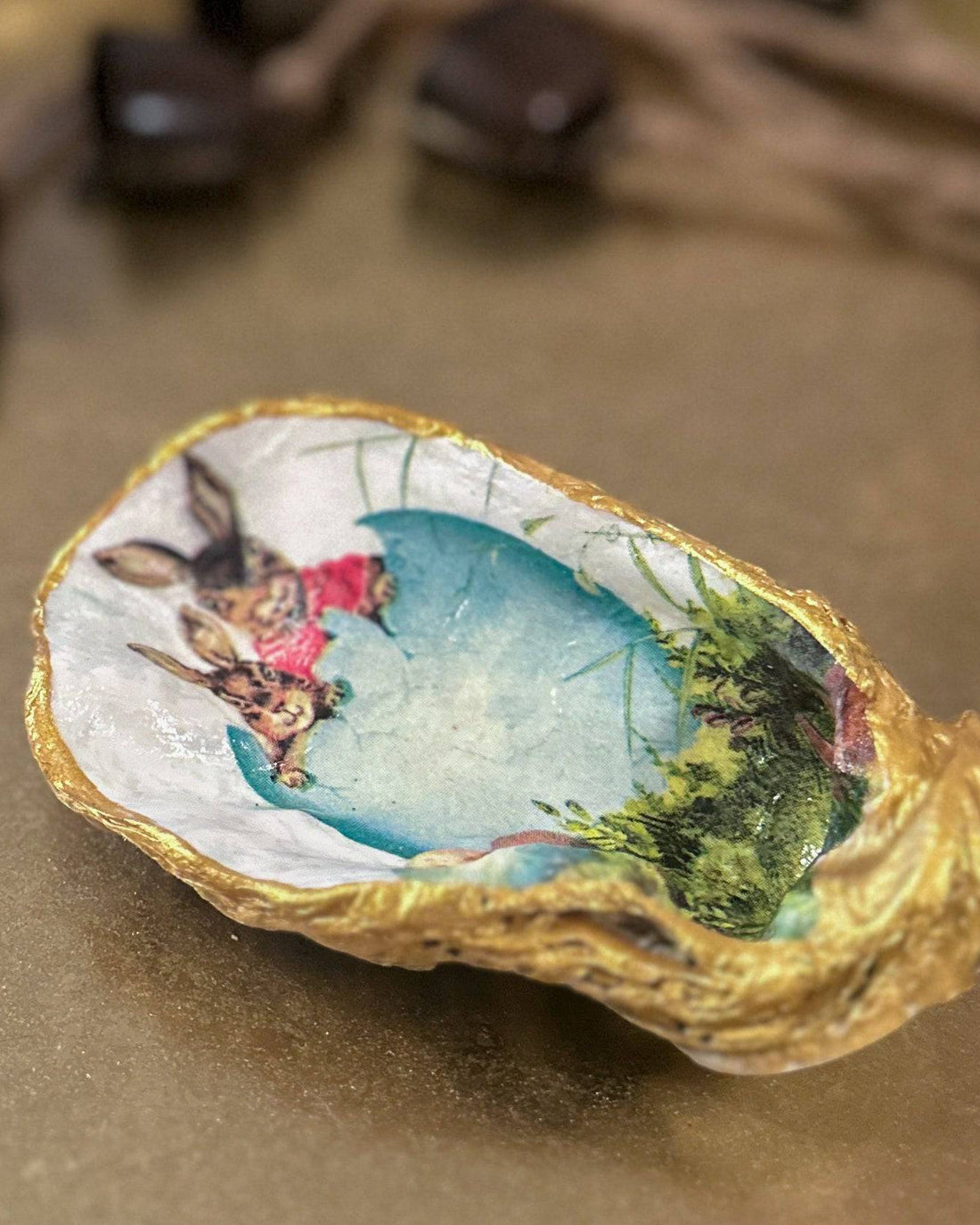 Handmade oyster shell trinket dish featuring an Easter bunny and open egg shell illustration, crafted with a decoupage technique and hand-painted gold edges, perfect for Easter or springtime gifts.