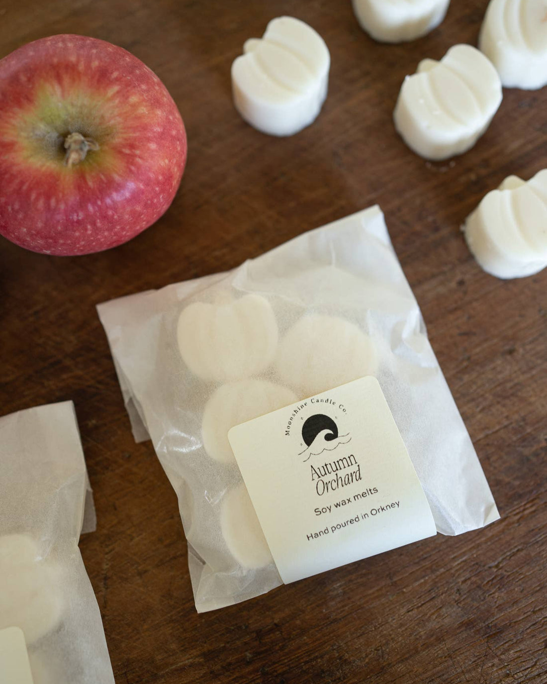 White wax melts in a clear package with a label, next to an apple on a wooden surface.