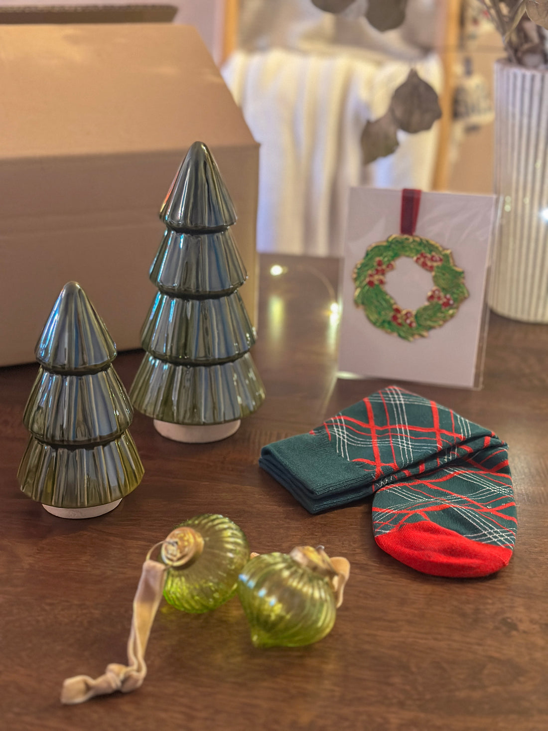 Christmas gift box with ceramic green tree ornaments, ribbed glass baubles, winter socks, and a tin wreath ornament. Ideal for festive gifting.