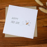 Handmade square birthday card featuring a bumblebee illustration with the words "Happy Bee-Day," printed on premium 100% recycled paper with a biodegradable cello wrap and Kraft envelope.