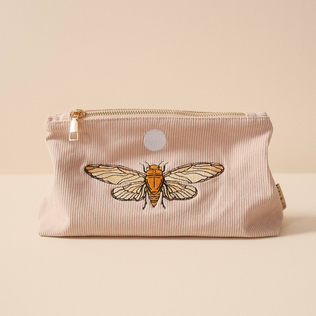 Medium pale pink corduroy pouch with a zip closure and embroidered designs of butterflies and flying insects. Fully lined for storing makeup, toiletries, or travel essentials.