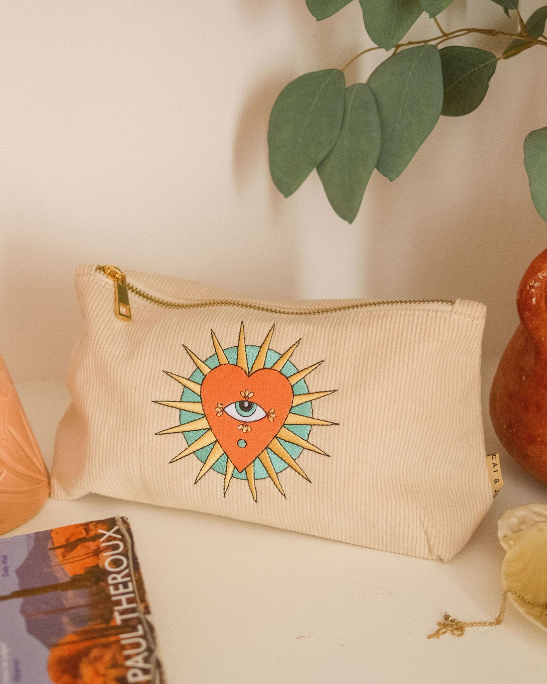 Stone-coloured medium corduroy pouch with a zip closure, featuring embroidered designs of a heart, eye, and sun. Fully lined for storing makeup, toiletries, or travel accessories.