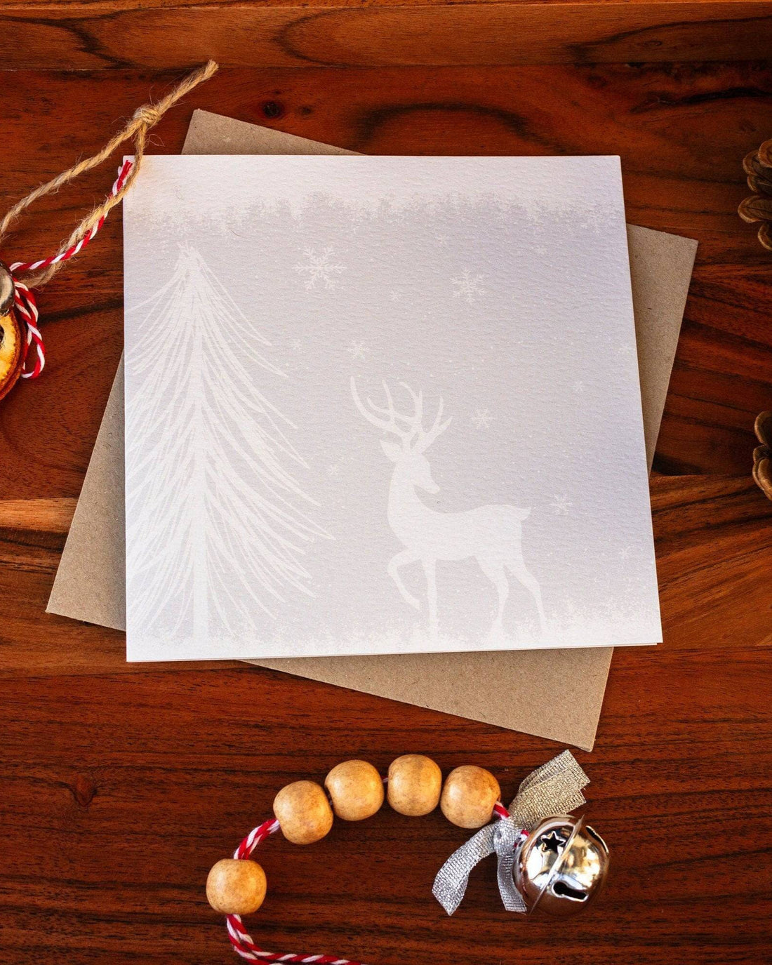 Square handmade Christmas card featuring a minimalist reindeer design in pale blue-grey tones with snow and trees, made with sustainably sourced textured paper and eco-friendly packaging.