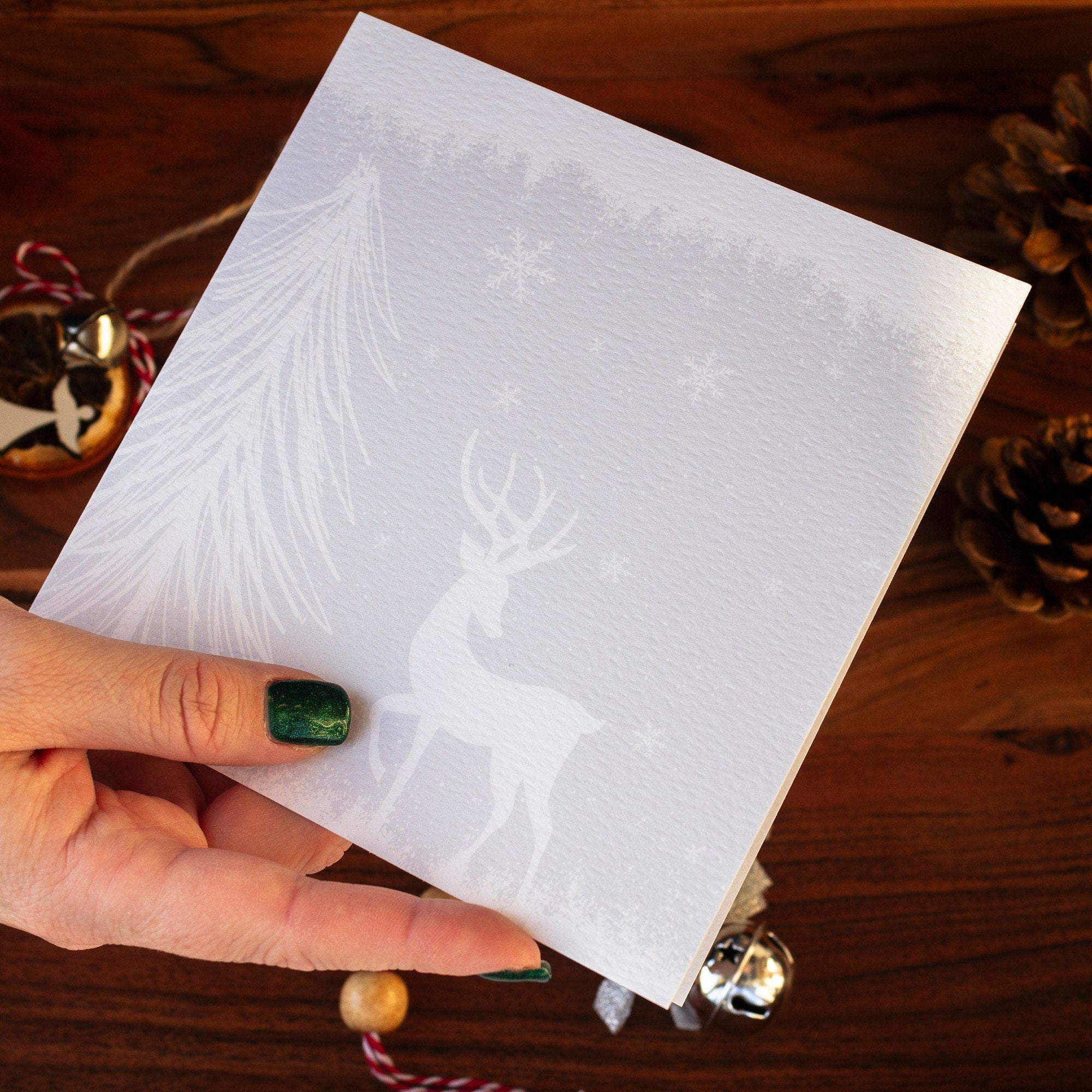 quare handmade Christmas card featuring a minimalist reindeer design in pale blue-grey tones with snow and trees, made with sustainably sourced textured paper and eco-friendly packaging.