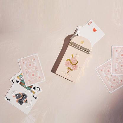 Premium-grade playing cards in pale pink with a gold-foiled tuck box featuring an ace of spades design with a snake wrapped around it. Perfect for games and gifting.