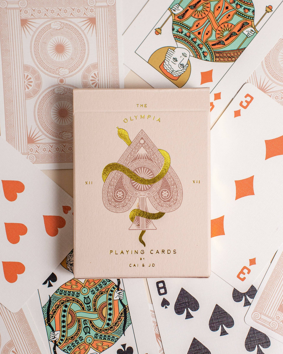 Premium-grade playing cards in pale pink with a gold-foiled tuck box featuring an ace of spades design with a snake wrapped around it. Perfect for games and gifting.