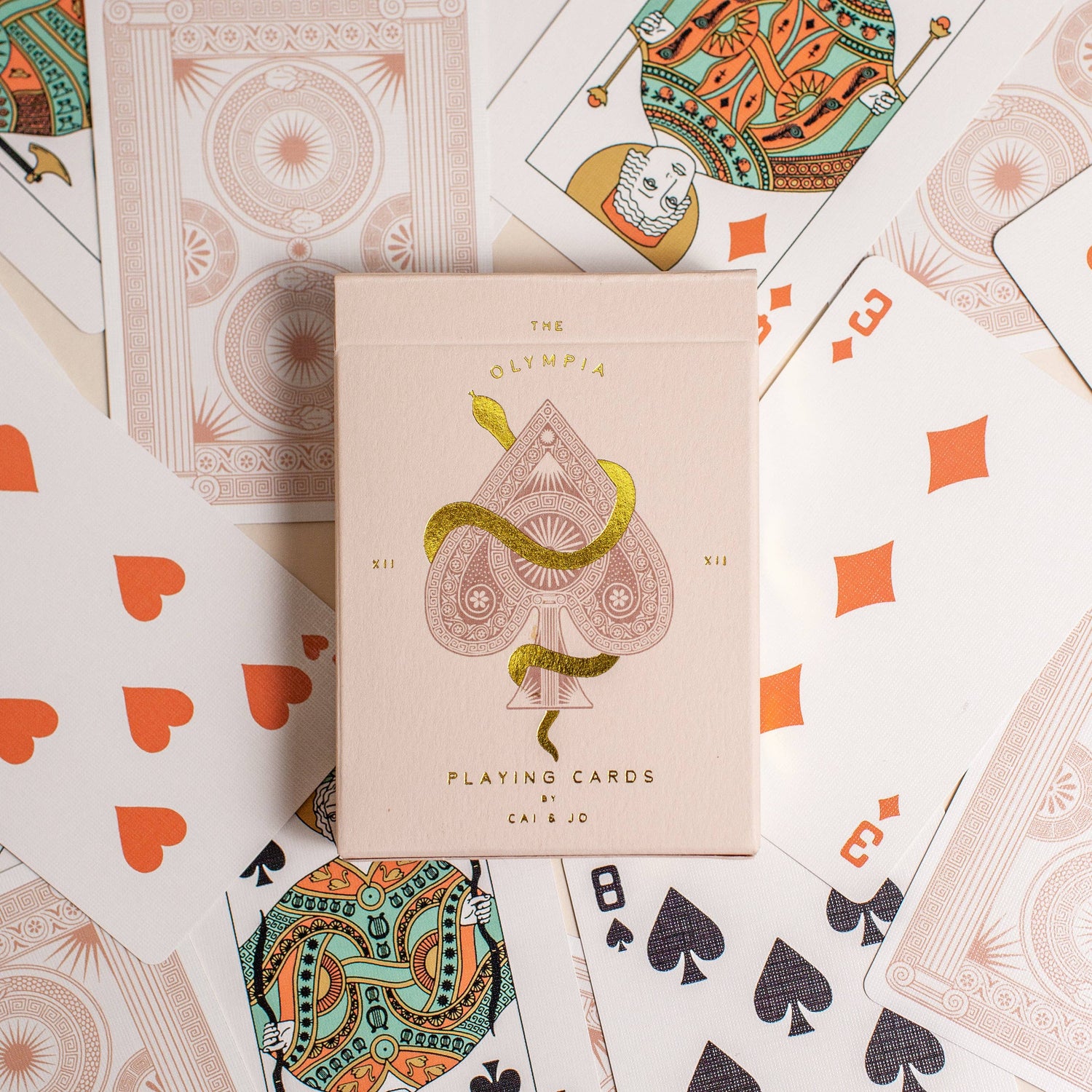 Premium-grade playing cards in pale pink with a gold-foiled tuck box featuring an ace of spades design with a snake wrapped around it. Perfect for games and gifting.