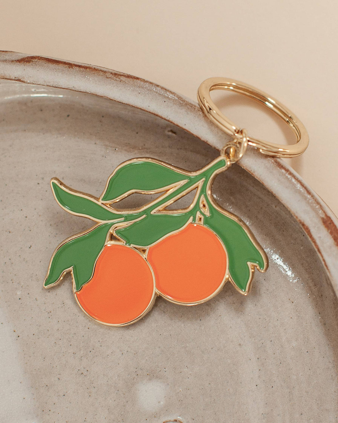 Soft enamel keychain with a design of two oranges and green accents, highlighted with gold details. Includes a matching gold ring.