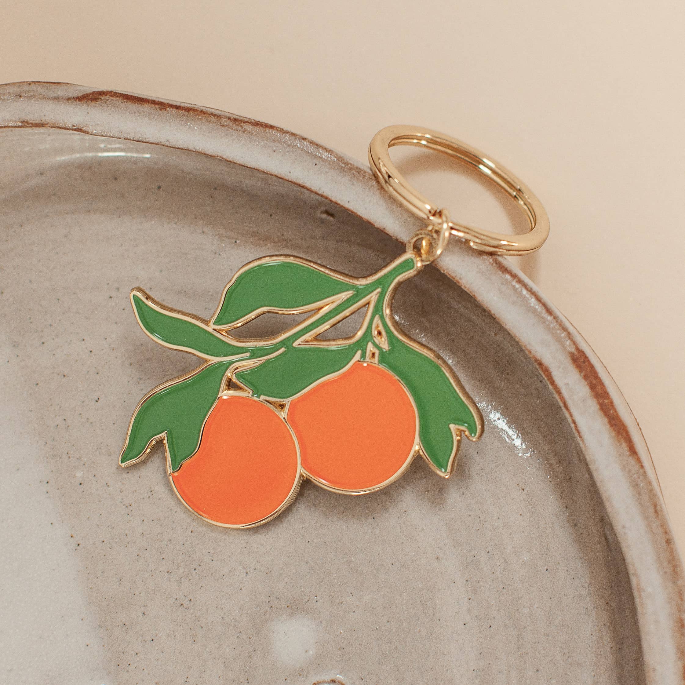 Soft enamel keychain with a design of two oranges and green accents, highlighted with gold details. Includes a matching gold ring.