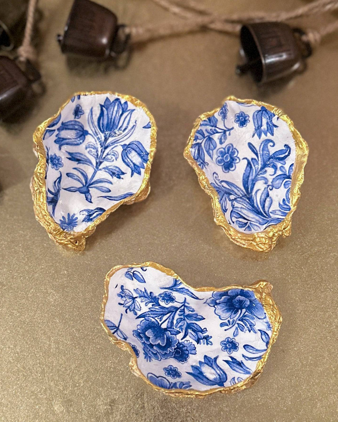 Set of three handmade oyster shell trinket dishes with blue and white floral designs, featuring a decoupage technique and hand-painted gold edges, ideal for home decor or jewellery storage.