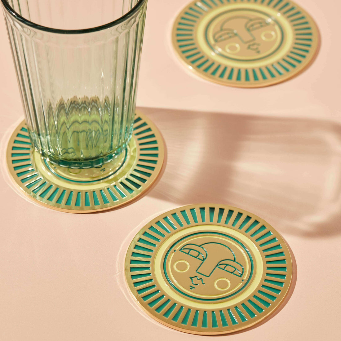 Round handmade teal coasters with gold-coloured metal and enamel, featuring the Sol face design. Perfect for home decor or barware.