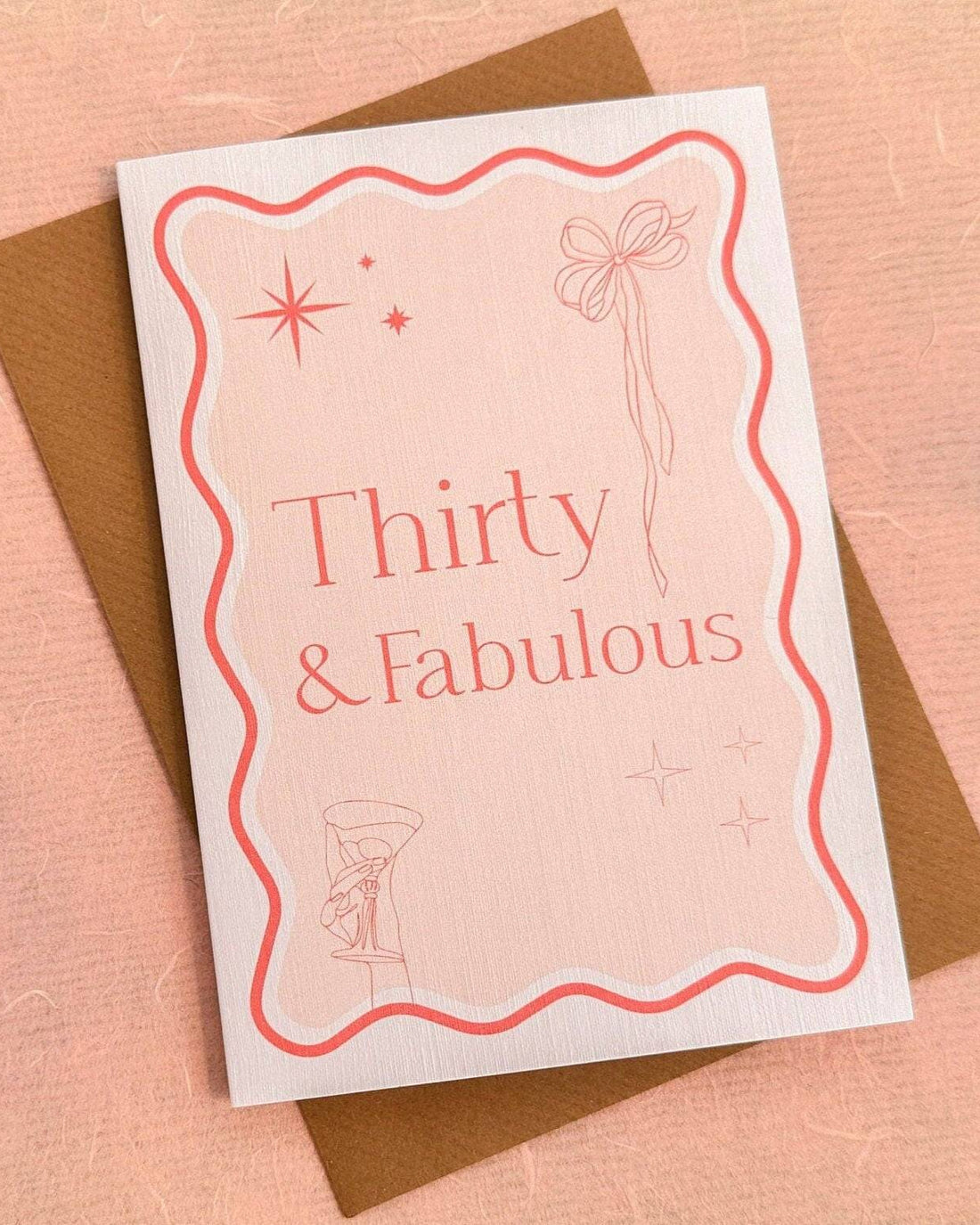 A6 handmade 30th birthday card featuring the words "Thirty & Fabulous" in pastel and bright pinks, with illustrations of a bow, stars, and cocktail. Includes a biodegradable cello wrap and Kraft envelope.