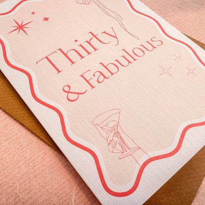 A6 handmade 30th birthday card featuring the words &quot;Thirty &amp; Fabulous&quot; in pastel and bright pinks, with illustrations of a bow, stars, and cocktail. Includes a biodegradable cello wrap and Kraft envelope.