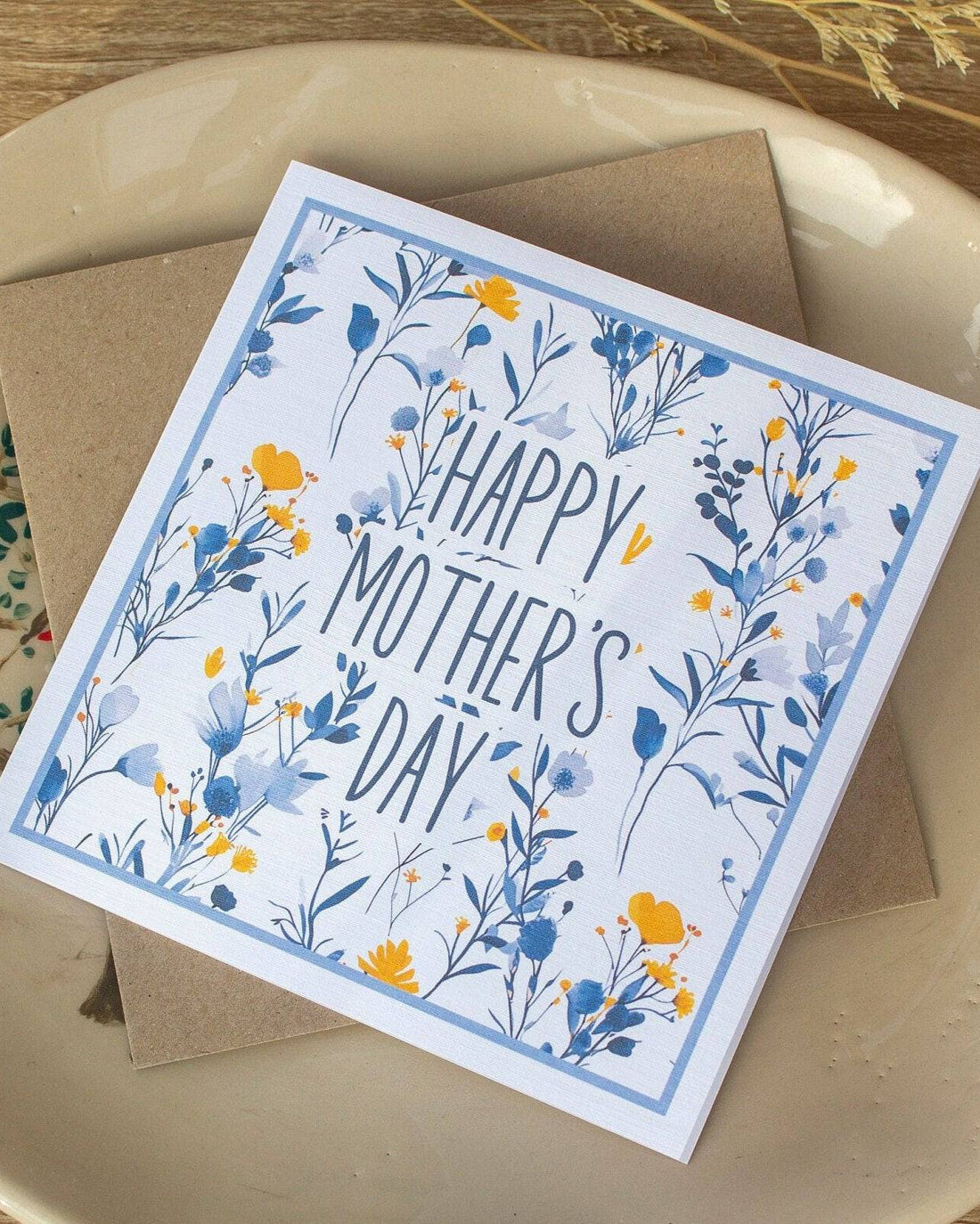 Square handmade Mother’s Day card featuring a vintage blue and yellow floral design with "Happy Mother’s Day" text in the centre. Packaged in a biodegradable cello wrap with a Kraft envelope.