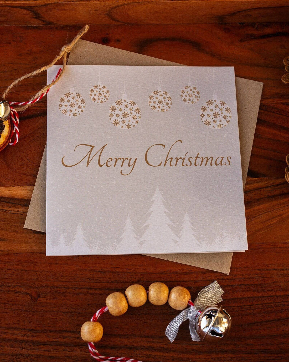 Square Christmas card with white snowy trees, hanging gold and white baubles, and "Merry Christmas" written in gold. Made from recyclable luxury textured paper with eco-friendly packaging.