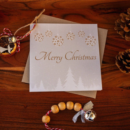 Square Christmas card with white snowy trees, hanging gold and white baubles, and &quot;Merry Christmas&quot; written in gold. Made from recyclable luxury textured paper with eco-friendly packaging.